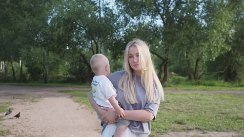 A Beautiful Young Mother with a Small Child in Her Arms Walks in the Park