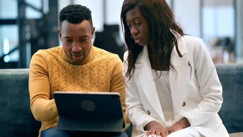Black man and woman working using a tablet in an office, discussing business affairs while sitting o