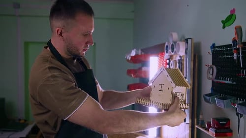 Carpenter Inspecting Small Wooden House Model in Workshop