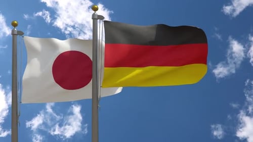 Japan and Germany Flags Waving on Flagpoles Against Blue Sky