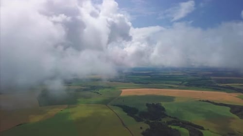 Aerial view of the fluffy clouds at summer sky. Flight over the rural areas with green summer fields