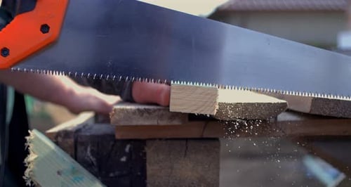 Hand sawing plank with orange handle saw, super slow motion at fps, close-up of precise
