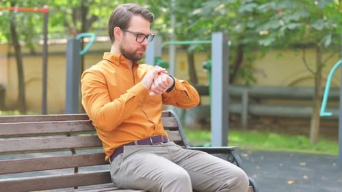 Man Checks Smartwatch While Sitting on Park Bench
