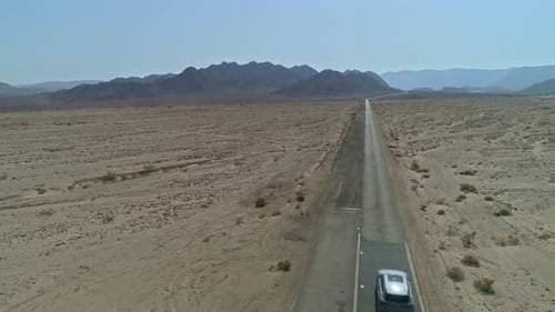 Aerial view of a fast sports car driving down a remote desert road