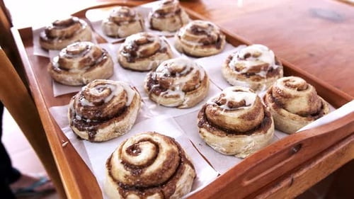 Frosting Being Drizzled Over Cinnamon Rolls on a Tray