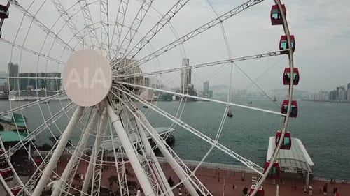 Foto aérea de uma roda gigante à beira-mar na cidade costeira contra o céu, drone subindo por estrutura - Hong
