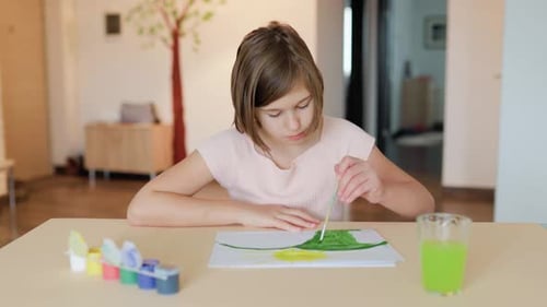 Front View of a Nice Serious Kid Girl Sitting at a Desk Drawing