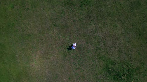 Woman raises arms to sky on green field. Aerial drone top-down ascending