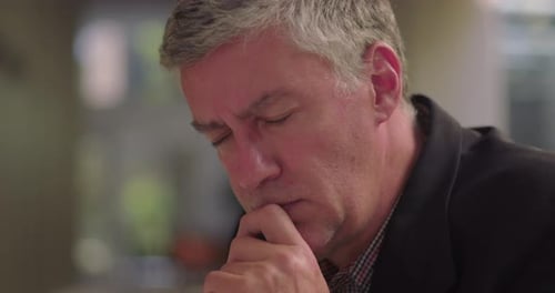 Close-up of middle aged man resting chin on hand in office lounge, deep in thought and focused
