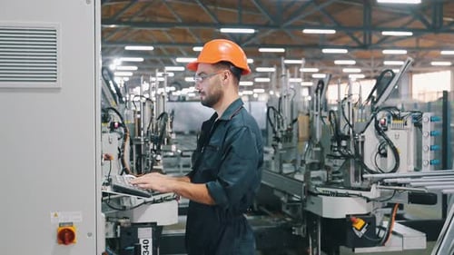 Adjusting settings of machine, operating. Factory worker is indoors with hard hat.