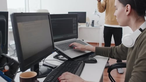 Woman Coding While Man Uses VR Headset in Office