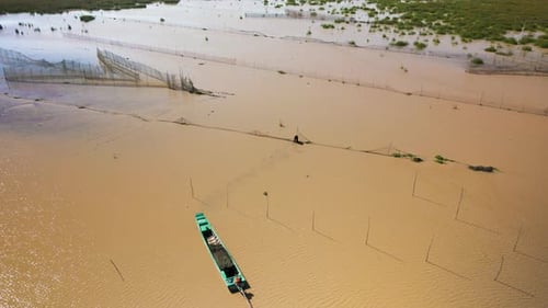 Aerial drone fly over of fisherman walks in shallow muddy water to fix netting on his arrow headed f
