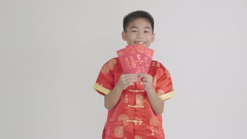 Frohes chinesisches Neujahrsfest, asiatischer Junge in einem roten Cheongsam Qipao, hält ein Geldgeschenk, roter Umschlag von Angpao