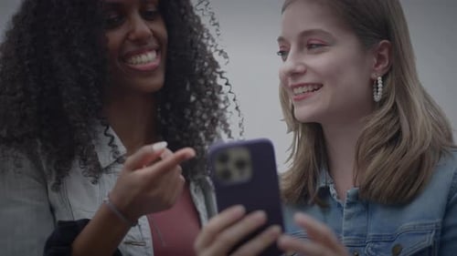 Two Smiling Women Sharing Content on Smartphone