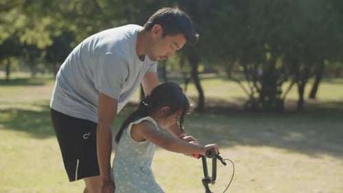 Happy Young Father Teaching His Daughter to Ride Bike in Park