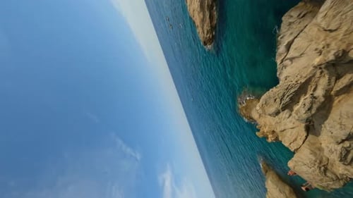 Vertikaler dynamischer FpV-Schuss die Klippe hinunter und fängt einen Kerl, der ins Wasser springt von