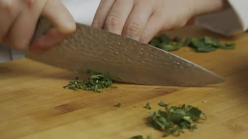 Chef slices mint leaves with kitchen knife on wooden cut board. Cooking vegetable salad. Slow motion