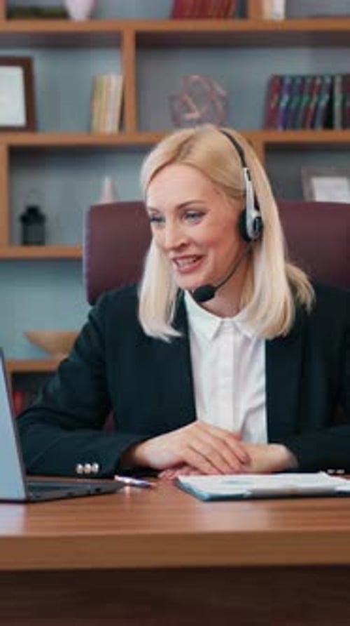 Pretty Positive Highskilled Effective Blond Female Office Manager Wears Headphones with Mic Sitting