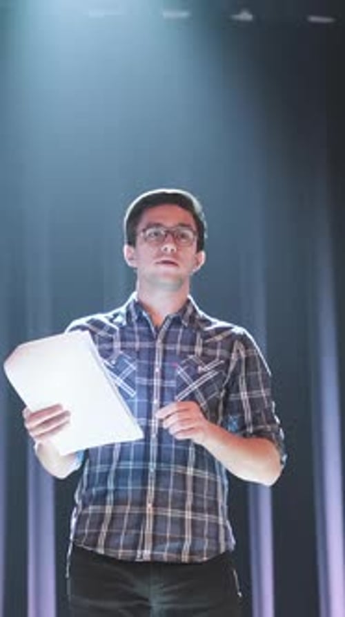 Young Man Reading Script Under Spotlight on Theater Stage