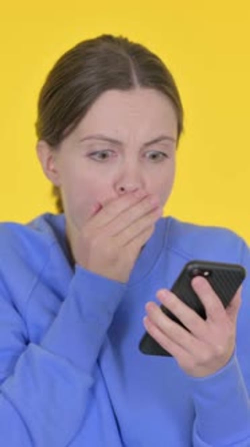 Shocked Young Woman Reacting to Phone on Yellow Background