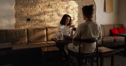 Woman Pours Tea for Friend at Cafe Table