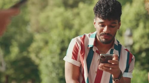 Close-up of young male sitting in park having picnic, talking with friends, using cellphone