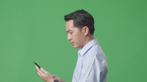 Side View Close Up Of Asian Business Man Using Mobile Phone While Walking On Green Screen
