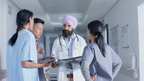 Diverse doctors and nurses using tablet and talking in corridor at hospital, in slow motion