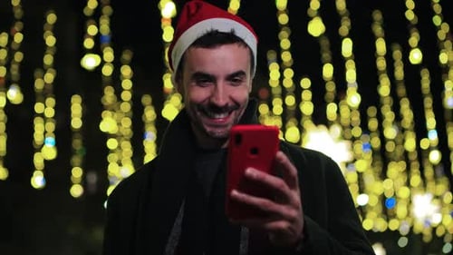Smiling Man in Santa Hat Uses Cell Phone