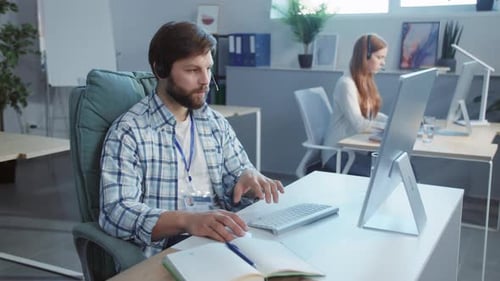 Un homme concentré à son bureau utilisant un casque et engagé dans le travail
