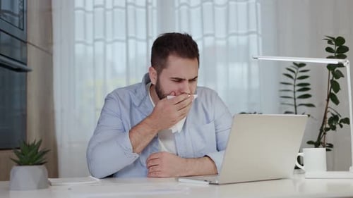 Man Blowing Nose Working at Home on Laptop