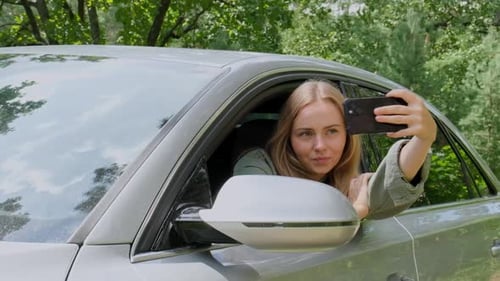 Blonde Frau hat auf der Straße ein Auto angehalten, um ein Selfie-Foto zu machen. Junge Touristin erkundet lokale Reisen