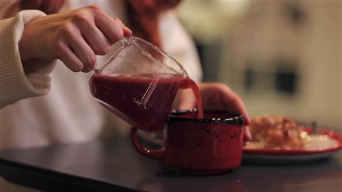 Woman Pours Red Drink into Mug Indoors
