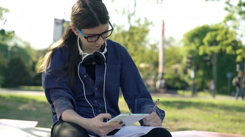 Teenage Girl with Smartphone Doing Homework Sitting in Park in City Alone