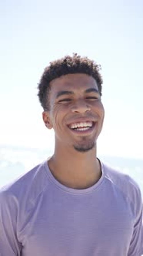 Vertical video: Smiling man enjoying sunny day at beach, wearing casual shirt
