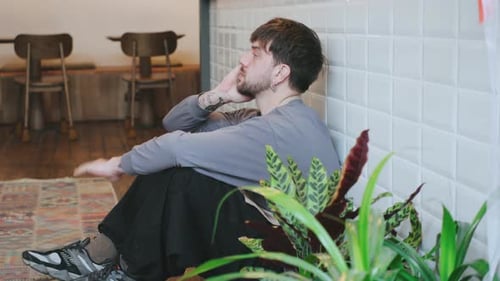 Tired Barista Takes a Break While Sitting on the Floor in a Cafe Showing a Moment of Fatigue During