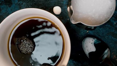Top view of coffee being poured in to white mug with circling bubbles on vibrant moody table