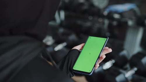 Young Muslim Female Athlete in a Hijab Using a Smartphone with a Mockup Green Screen to Improve Her