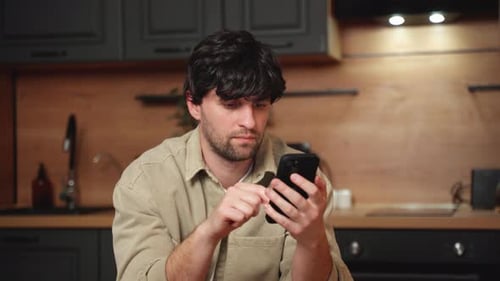 Young Man Using Smartphone in Modern Kitchen