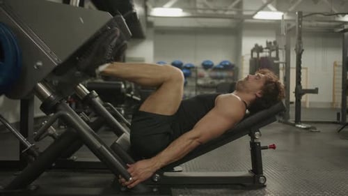 Muscular Man Performing Leg Press Exercise on Gym Machine
