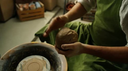 A potter works clay on a potter's wheel A potter forms a clay product using pottery tools