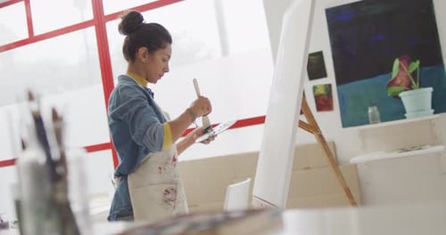 Video of biracial female artist painting in studio