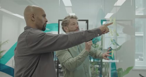 Two Businessmen in Casual Office Meeting, Sticking Notes on Glass wall