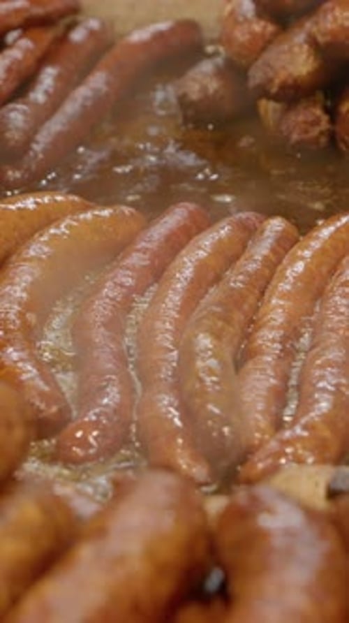 Vertical video Juicy sausages frying on hot plate in street food market