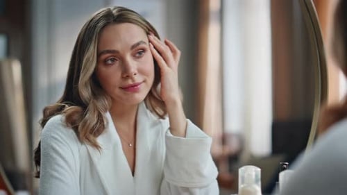 Woman in White Robe Examines Skin in Mirror