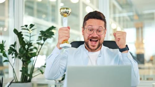 Excited Businessman Celebrates Online Victory with Trophy in Office