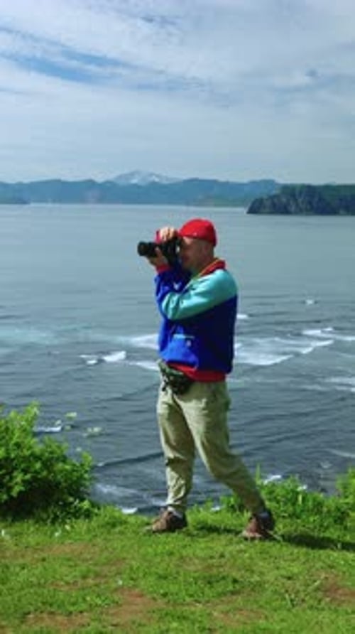 A Photographer Captures Breathtaking Coastal Scenery Poised on a Cliff with a Camera in Hand