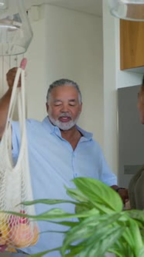 Vídeo vertical: Entrando a casa, hombre cargando bolsas, levantando una bolsa de malla en la isla, clasificando la comida