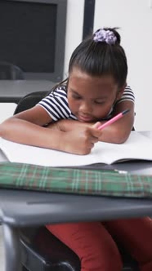 Vertical video: In school setting, young African American girl is focused on writing