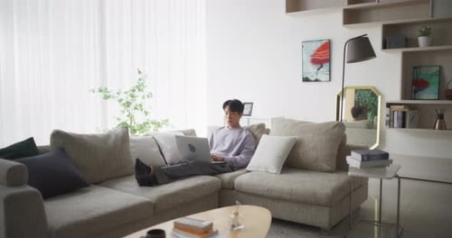 Young Adult Relaxing with Laptop on Sofa at Home